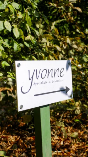 Bordje 'Yvonne, Specialiste in Schoonheid' bij de ingang van de salon